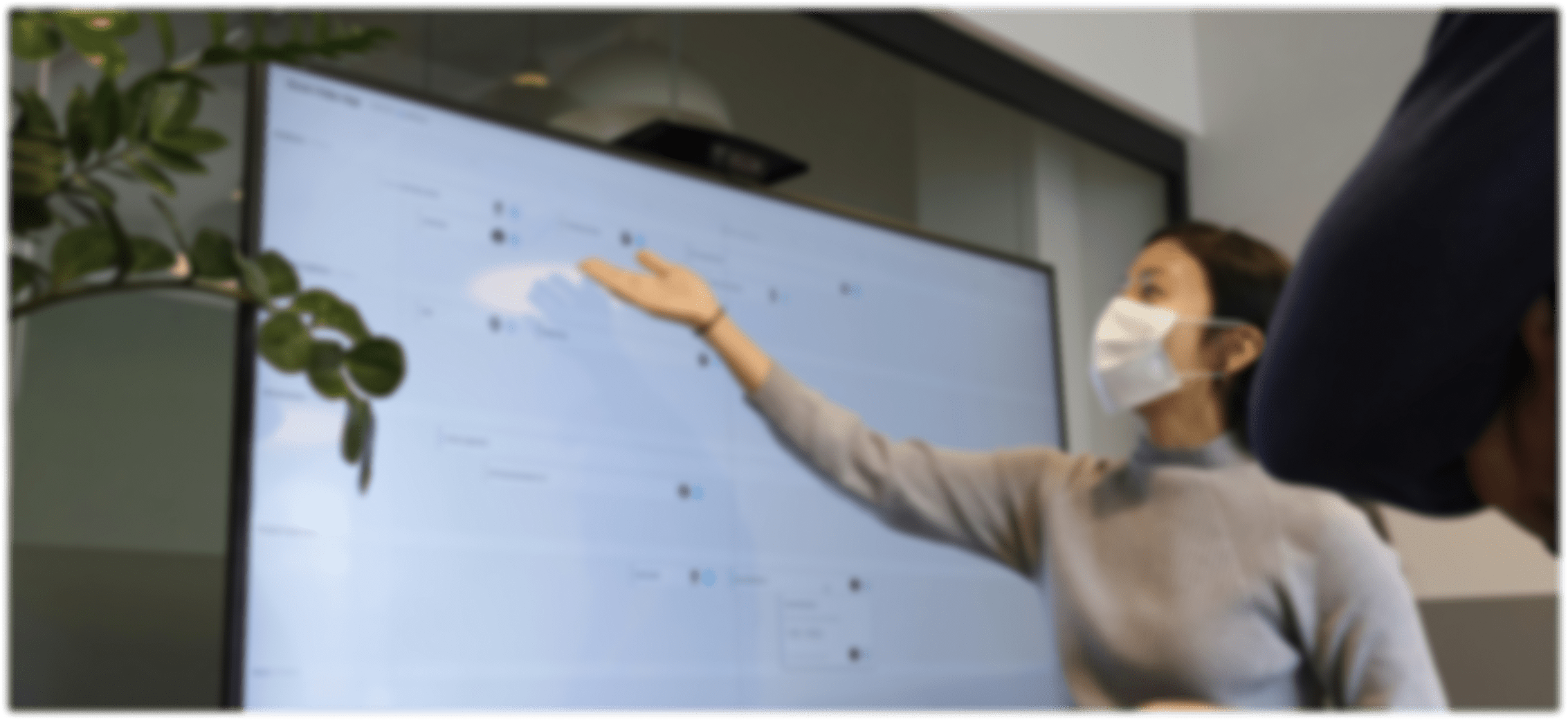 A woman wearing a face mask points at a screen.