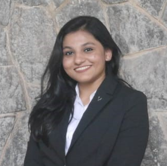 A woman standing in front of a wall wearing blue suit.